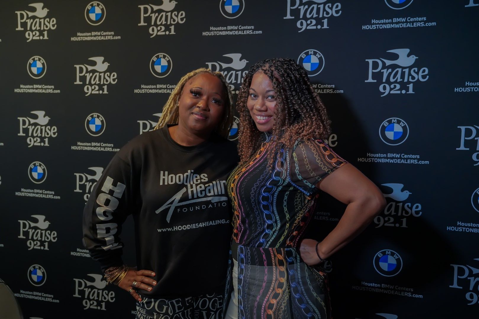 Two women are posing for a picture in front of a wall with bmw logos.
