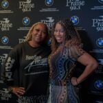 Two women are posing for a picture in front of a wall with bmw logos.