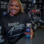 A woman wearing a black hoodie is sitting at a table holding a can of pepsi.