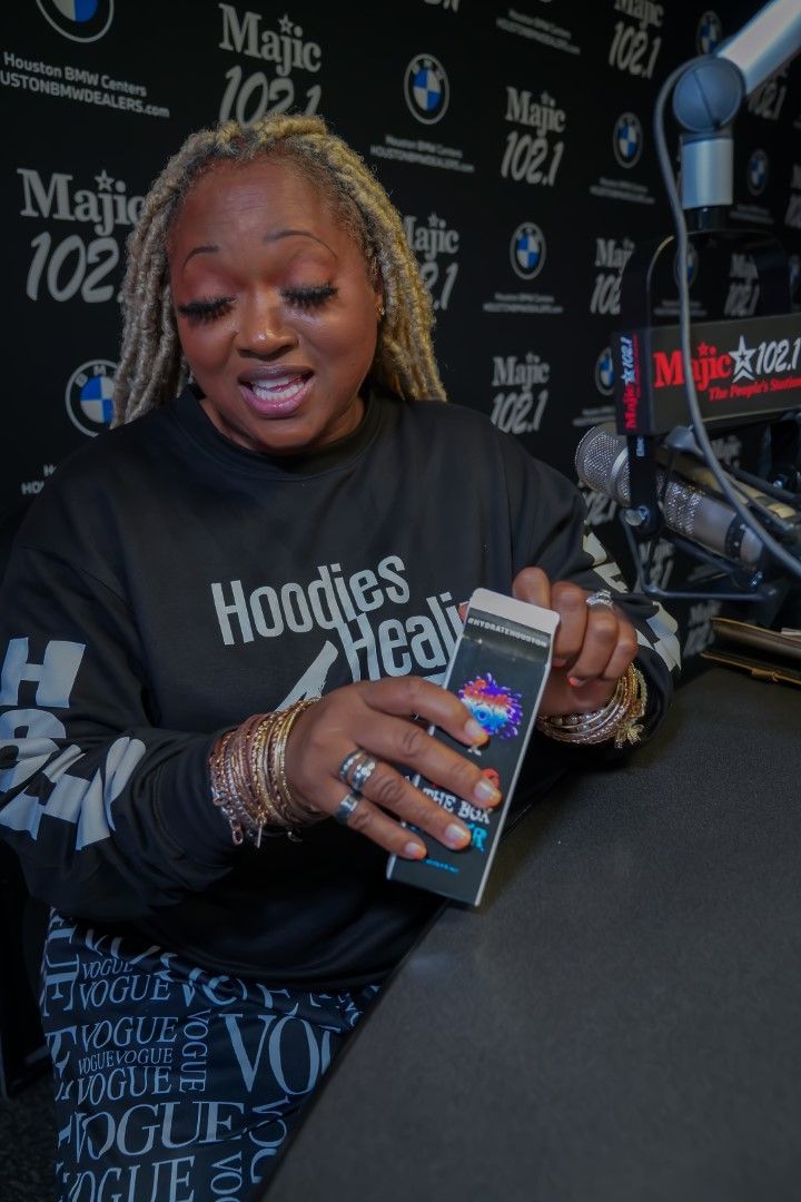A woman is sitting at a desk in front of a microphone holding a cell phone.