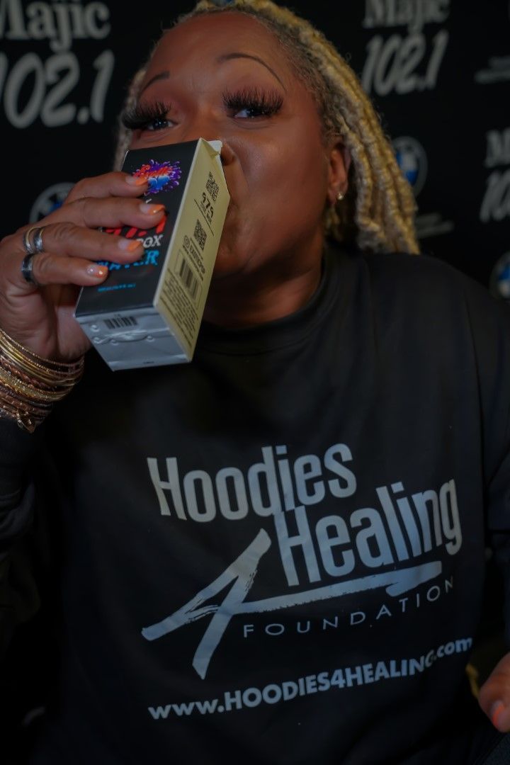 A woman wearing a black shirt that says hoodies healing drinking from a box