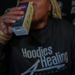 A woman in a hoodie is drinking from a box.