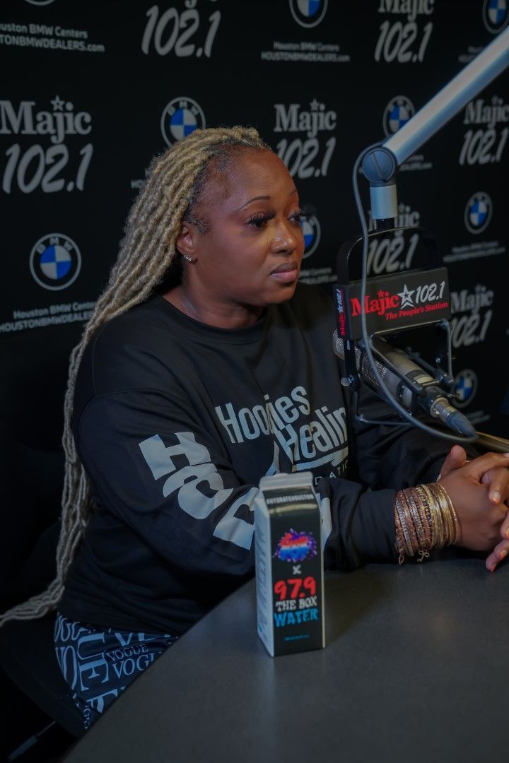 A woman is sitting at a table in front of a microphone wearing a shirt that says homies real