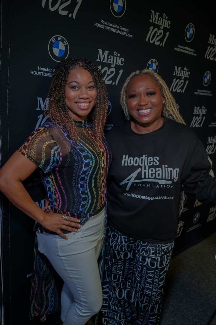 Two women are posing for a picture in front of a black wall.