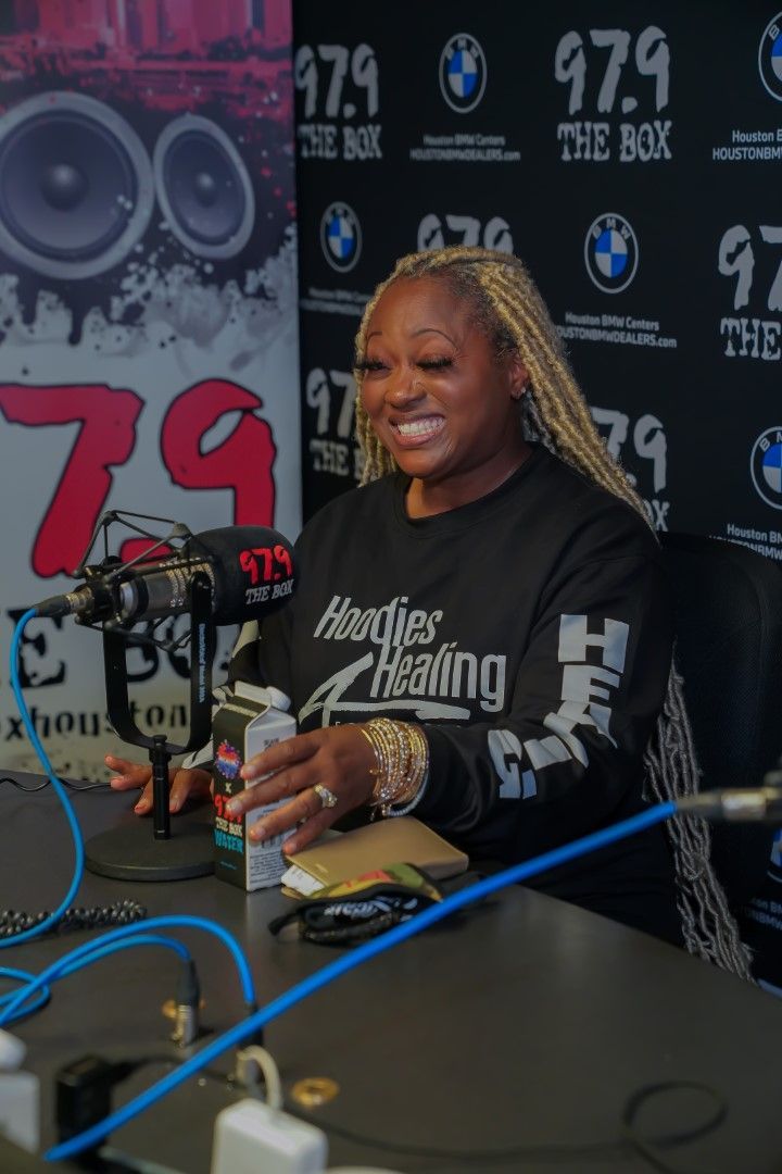A woman is sitting at a table in front of a microphone wearing a shirt that says heather healing