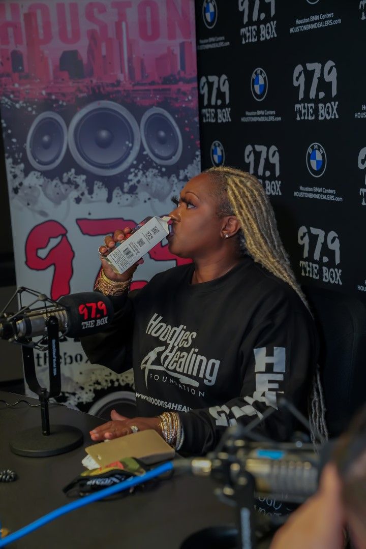 A woman drinking from a bottle in front of a sign that says 97.9