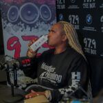 A woman is sitting in front of a microphone drinking from a bottle.