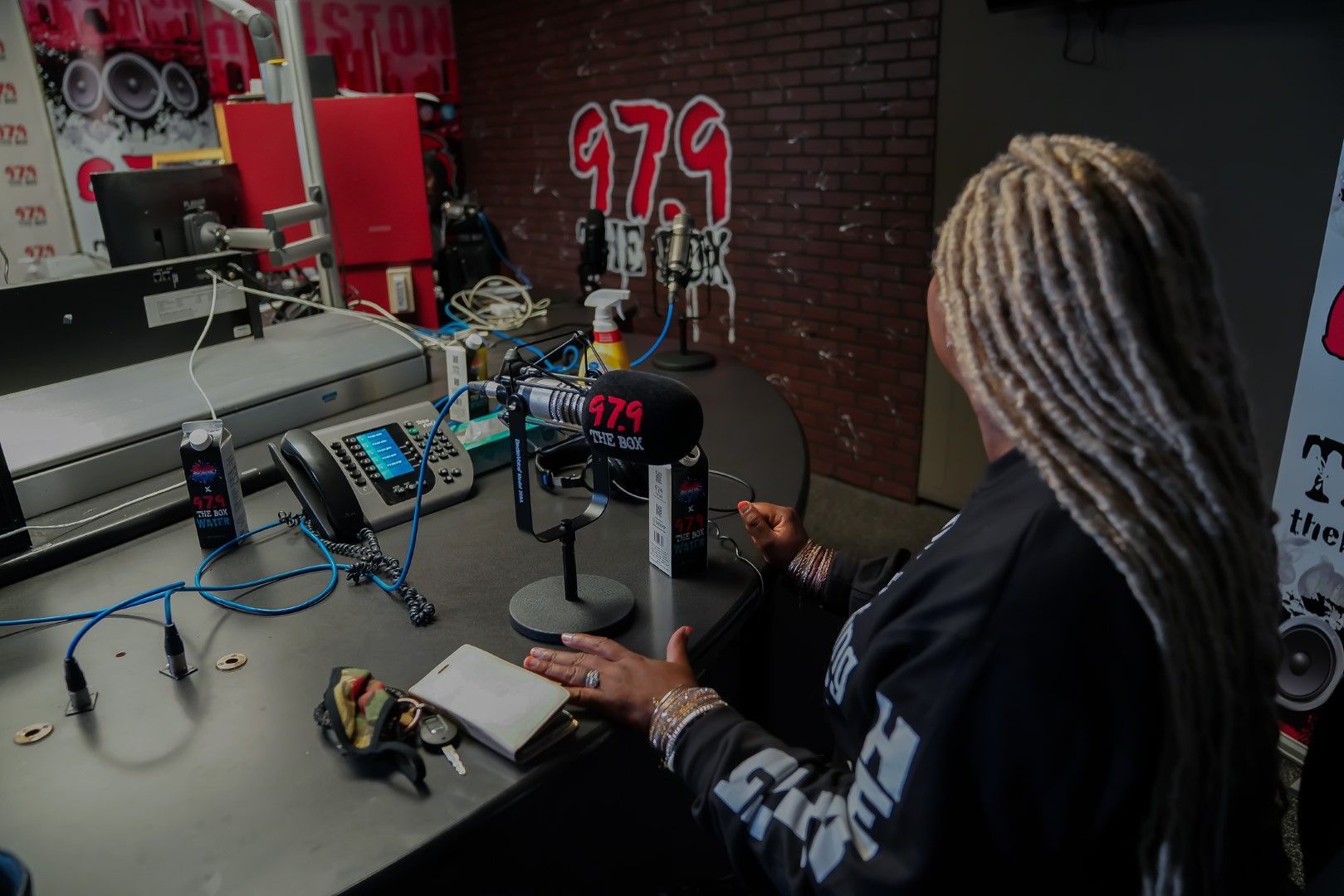 A woman with dreadlocks is sitting at a desk in front of a microphone.