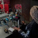 A woman is sitting at a desk in front of a microphone.