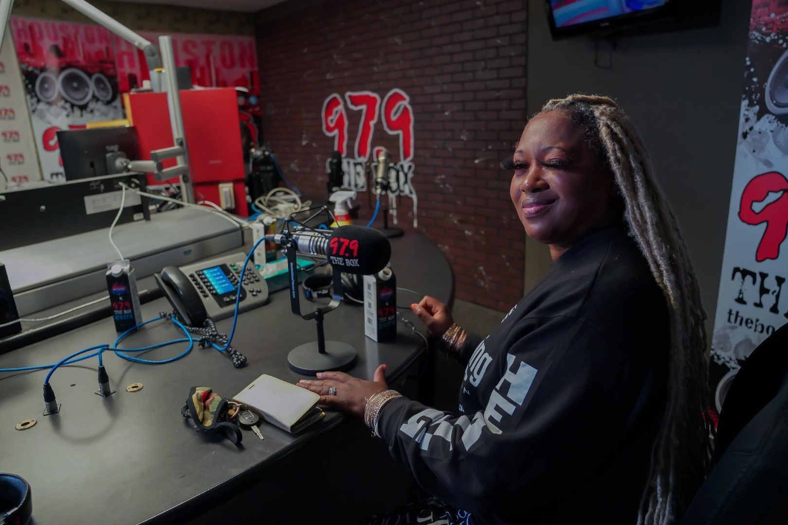 A woman is sitting at a desk in front of a microphone in a radio station.