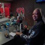 A woman is sitting at a desk in front of a microphone in a radio station.