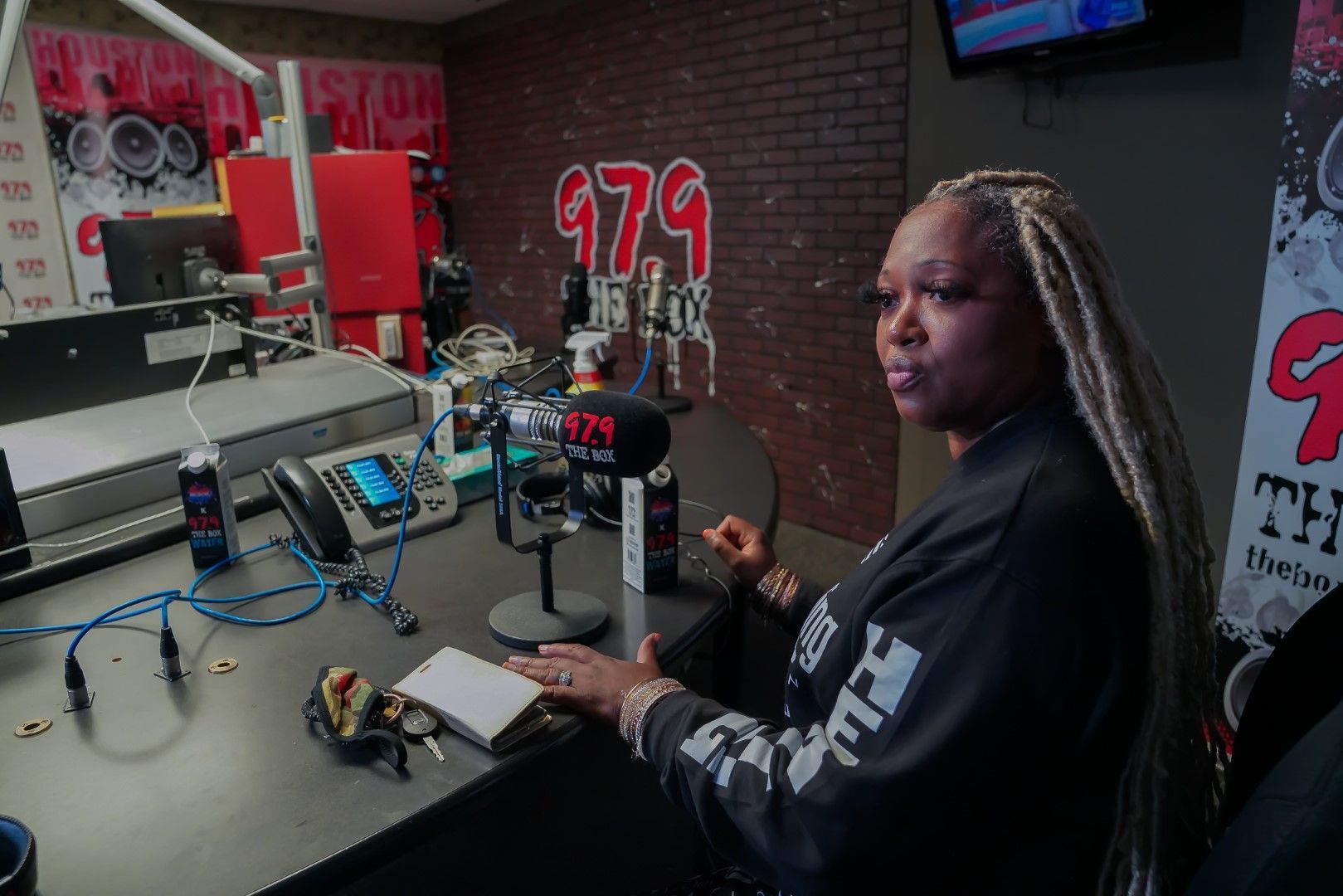 A woman is sitting at a desk in front of a microphone in a radio station.