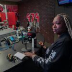 A woman is sitting at a desk in front of a microphone in a radio station.