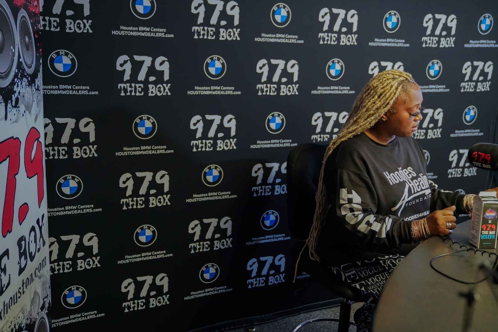 A woman is sitting in front of a wall with a bmw logo on it.