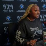 A woman is sitting in front of a microphone wearing a black sweatshirt.