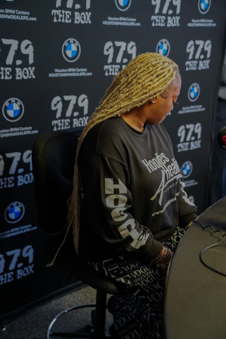 A woman is sitting at a table in front of a wall that says 97.9 the box