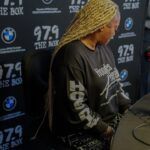 A woman with blonde braids is sitting at a desk in front of a microphone.
