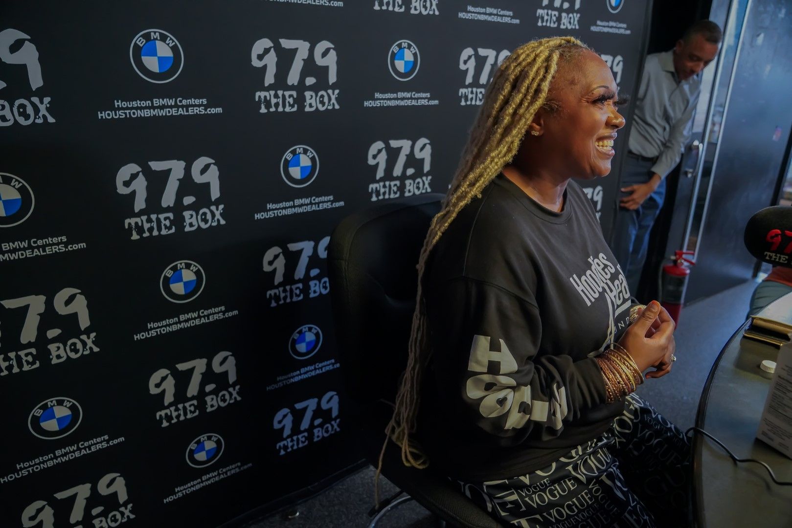 A woman is sitting in front of a wall that says 97.9 the box.
