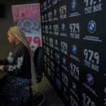 A woman is sitting in front of a large black wall.