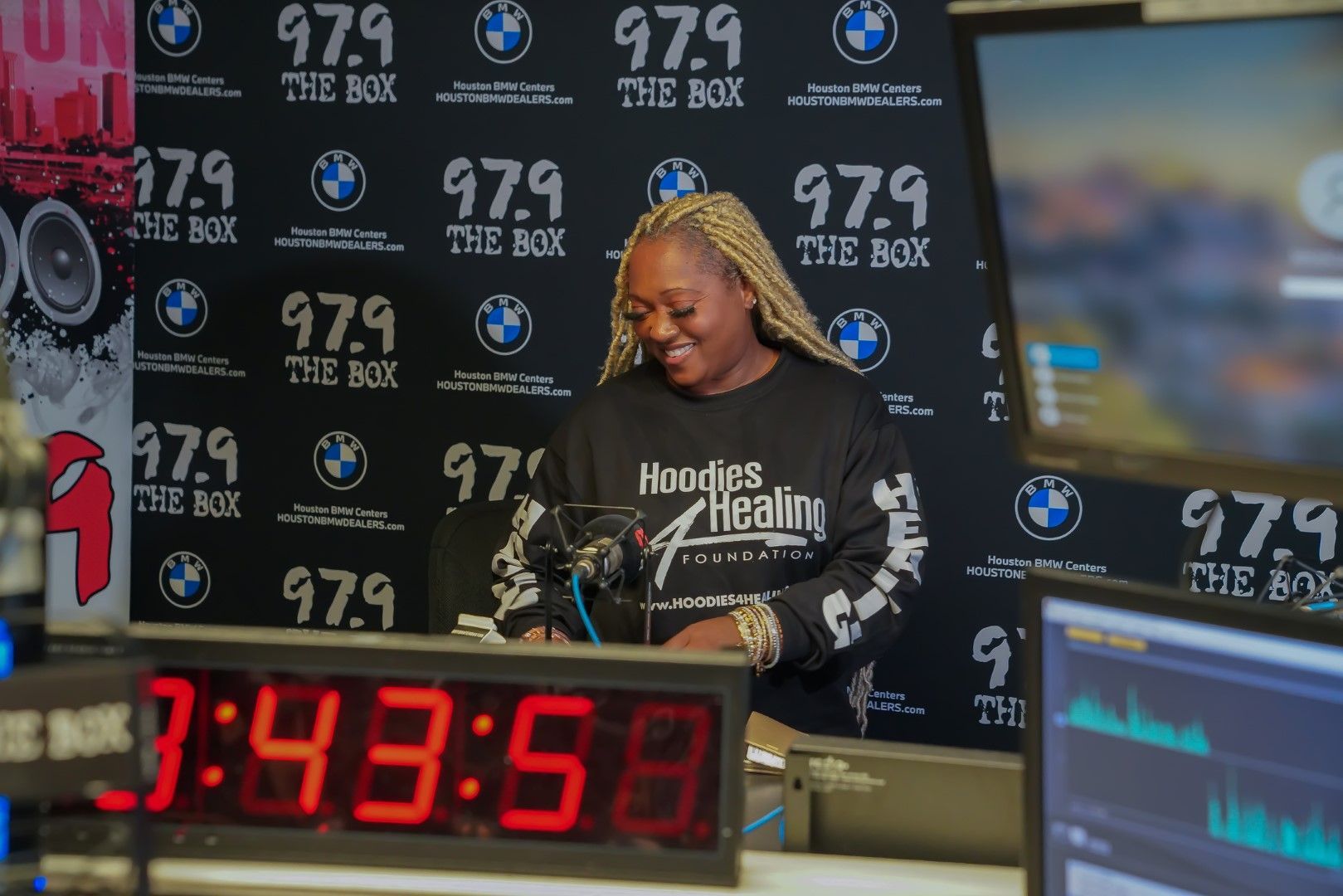 A woman is sitting at a desk in front of a digital clock.