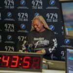 A woman is sitting at a desk in front of a clock.