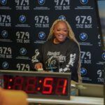 A woman is sitting at a desk in front of a clock.