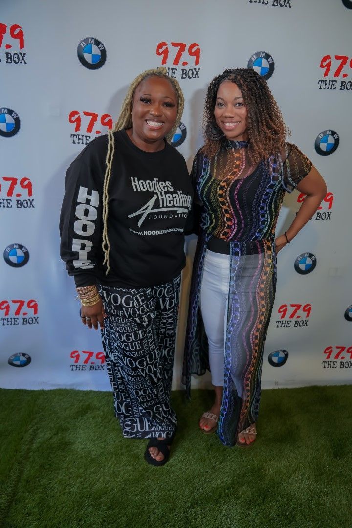 Two women are posing for a picture in front of a bmw backdrop.