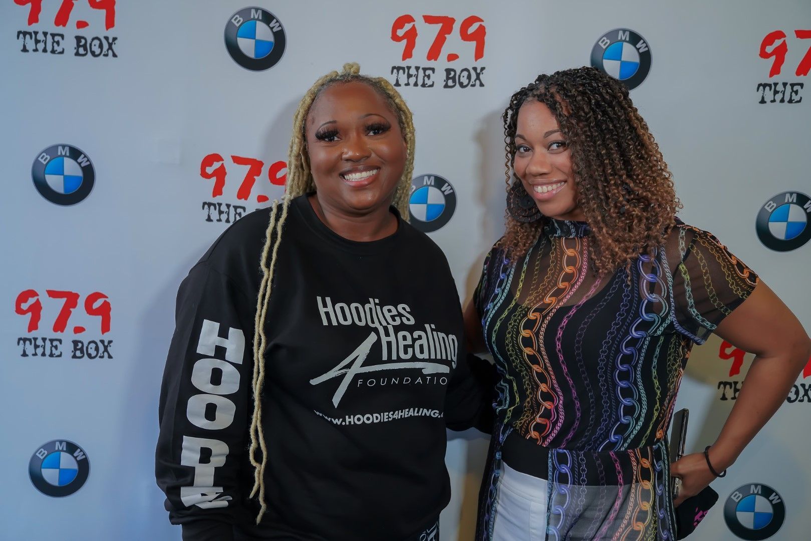 Two women are posing for a picture in front of a backdrop that says 97.9 the box