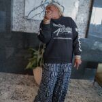 A man is standing in a living room wearing a black sweatshirt and blue pants.