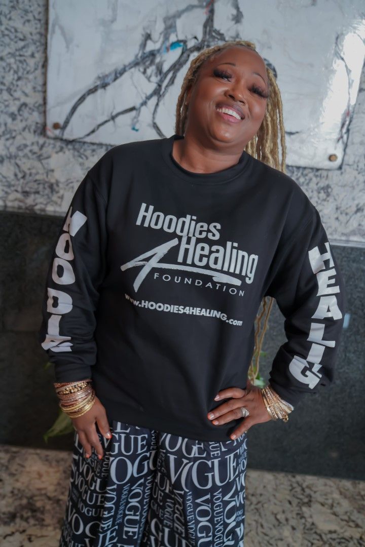 A woman is wearing a black hoodie that says hoodies healing foundation.