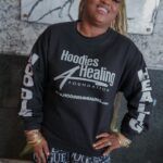 A woman is wearing a black sweatshirt with the words `` hoodies healing '' on the sleeves.