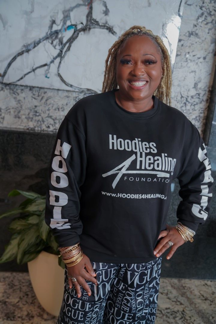 A woman wearing a black sweatshirt that says hoodies healing foundation