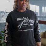 A woman wearing a black hoodie is standing in a room.