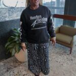 A woman is standing in a room wearing a black sweatshirt and pants.