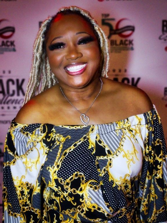 A woman is smiling in front of a sign that says black