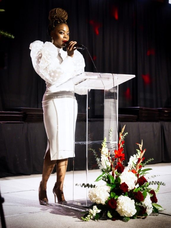 A woman in a white dress is standing at a podium and singing into a microphone.