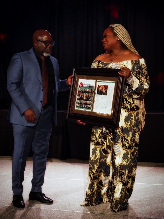 A man in a suit stands next to a woman holding a framed picture