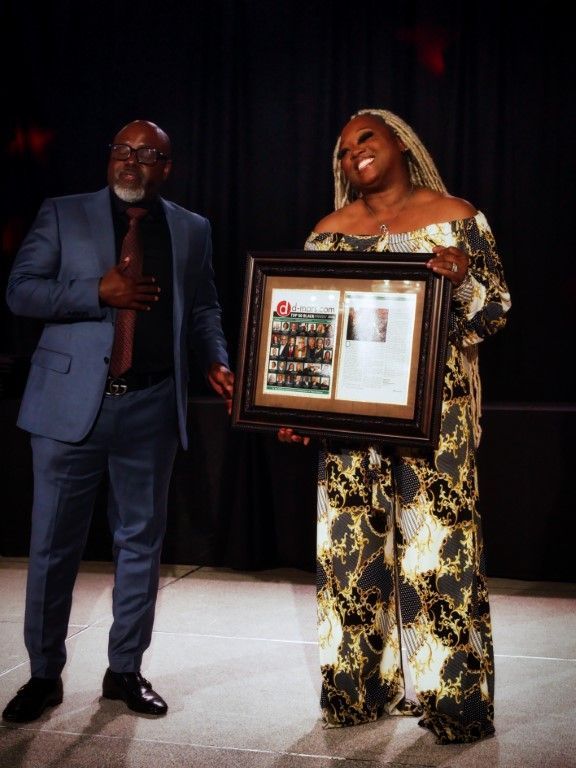 A man in a suit stands next to a woman holding a framed picture