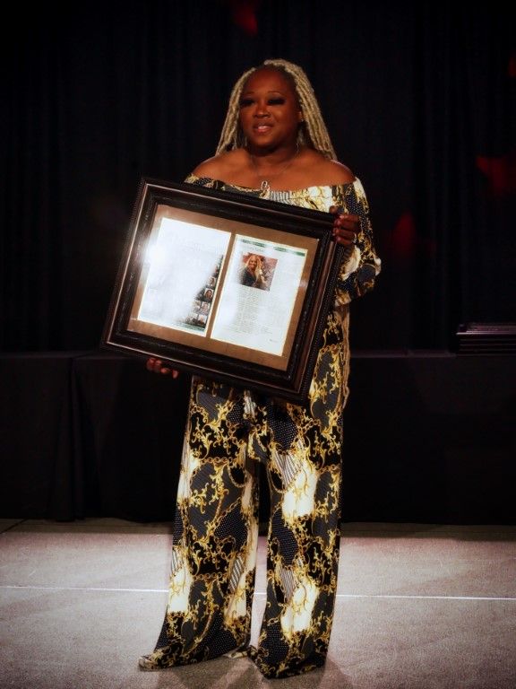 A woman in a gold and black jumpsuit is holding a framed picture.