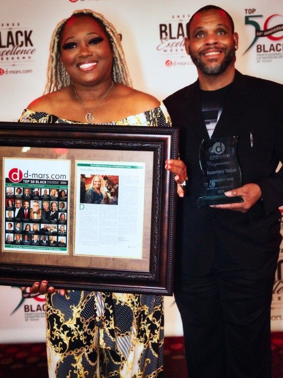 A man and a woman holding framed awards in front of a wall that says black excellence