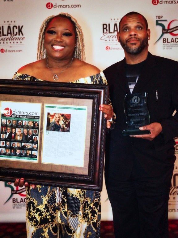 A man and a woman holding framed pictures in front of a wall that says black