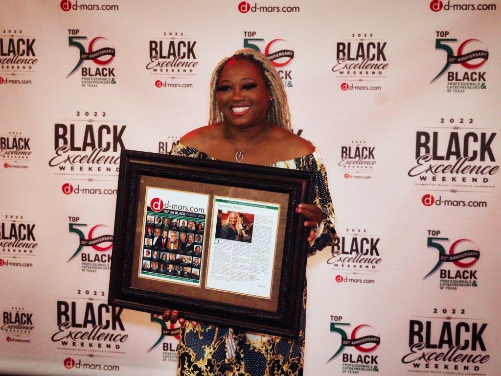 A woman is holding a framed picture in front of a wall that says black excellence