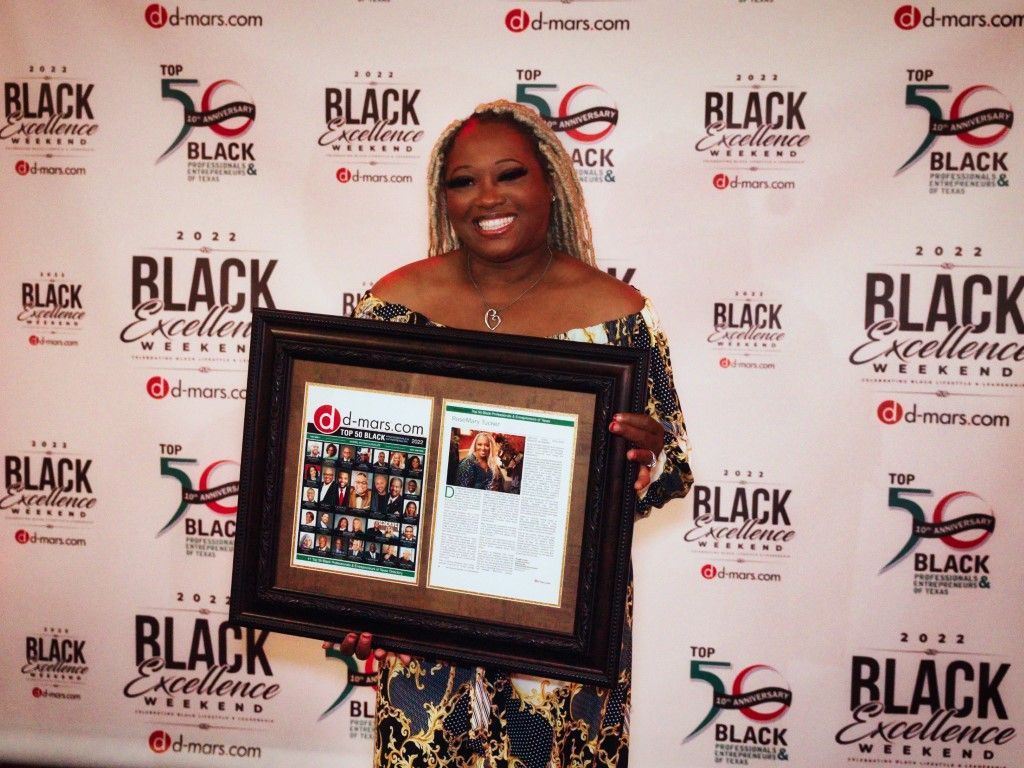 A woman is holding a framed picture in front of a wall that says black excellence