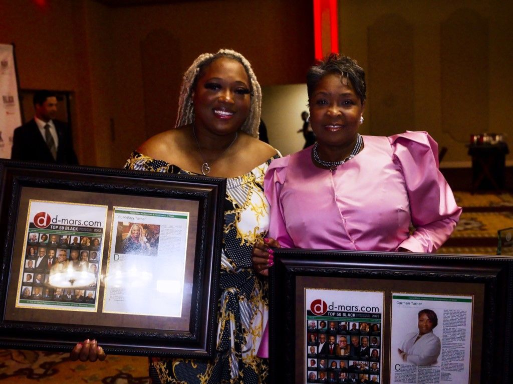 Two women are posing for a picture while holding framed pictures