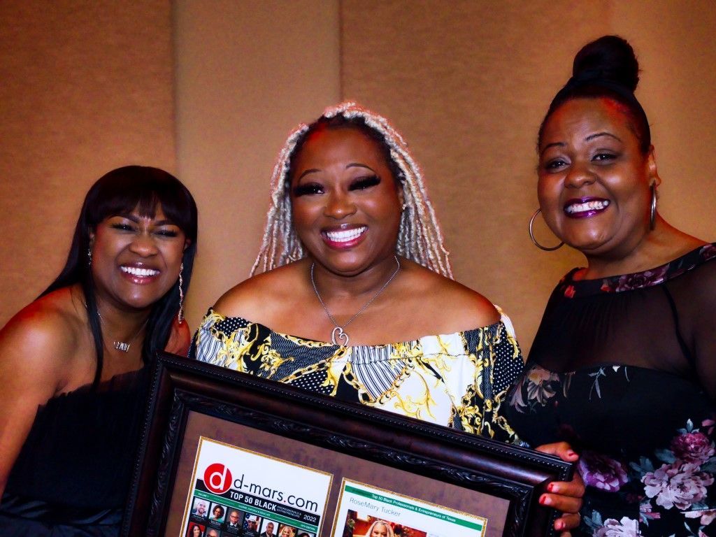 Three women are posing for a picture and one of them is holding a framed picture