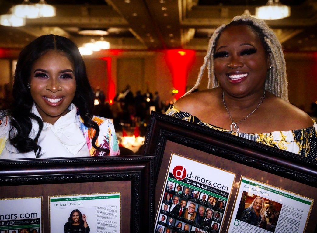 Two women are holding framed pictures and smiling at the camera.