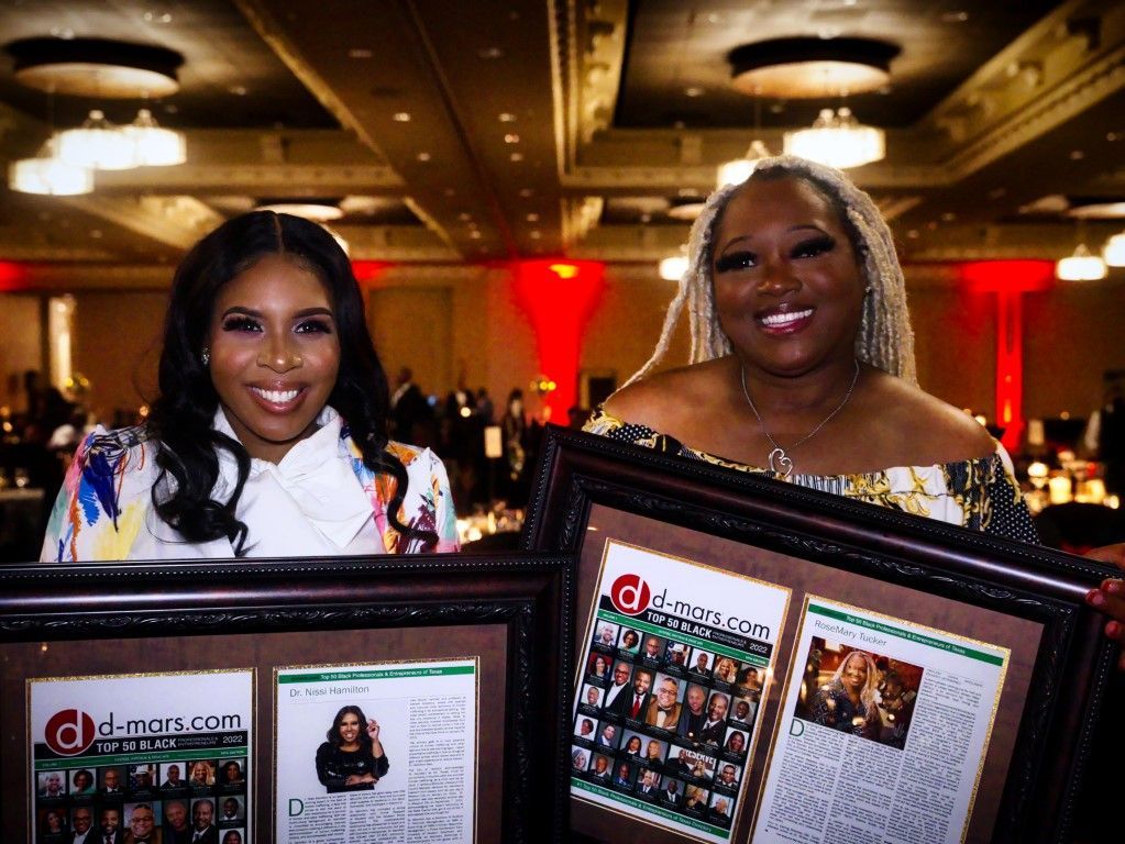 Two women are standing next to each other holding framed pictures.