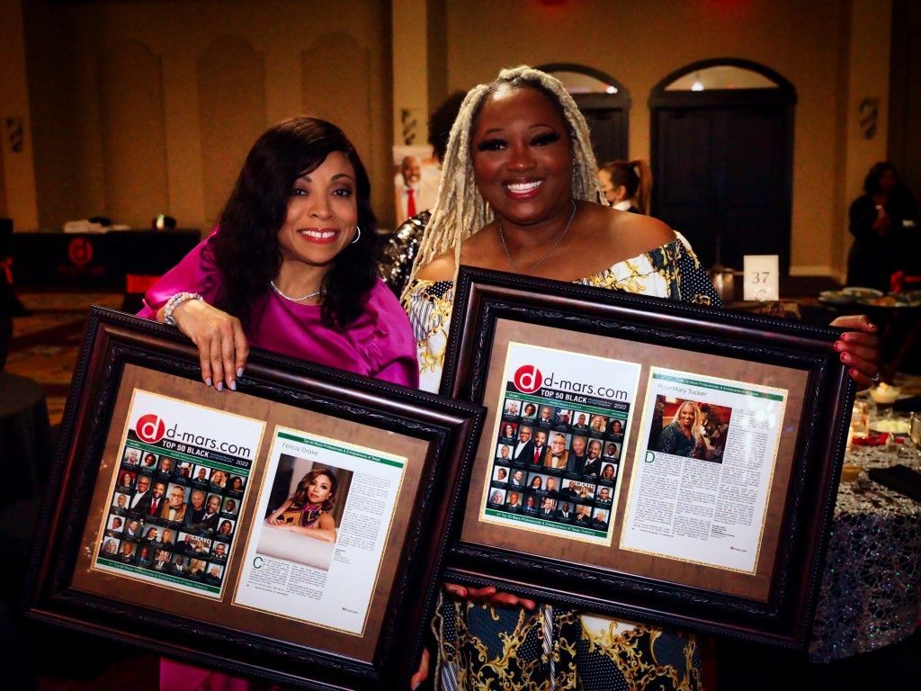 Two women are posing for a picture while holding framed pictures