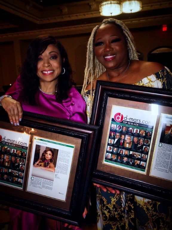 Two women are holding framed pictures and one of them is wearing a pink dress