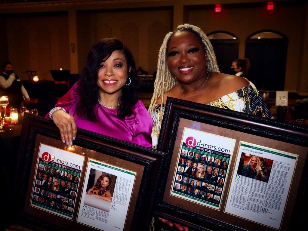 Two women are posing for a picture while holding framed pictures